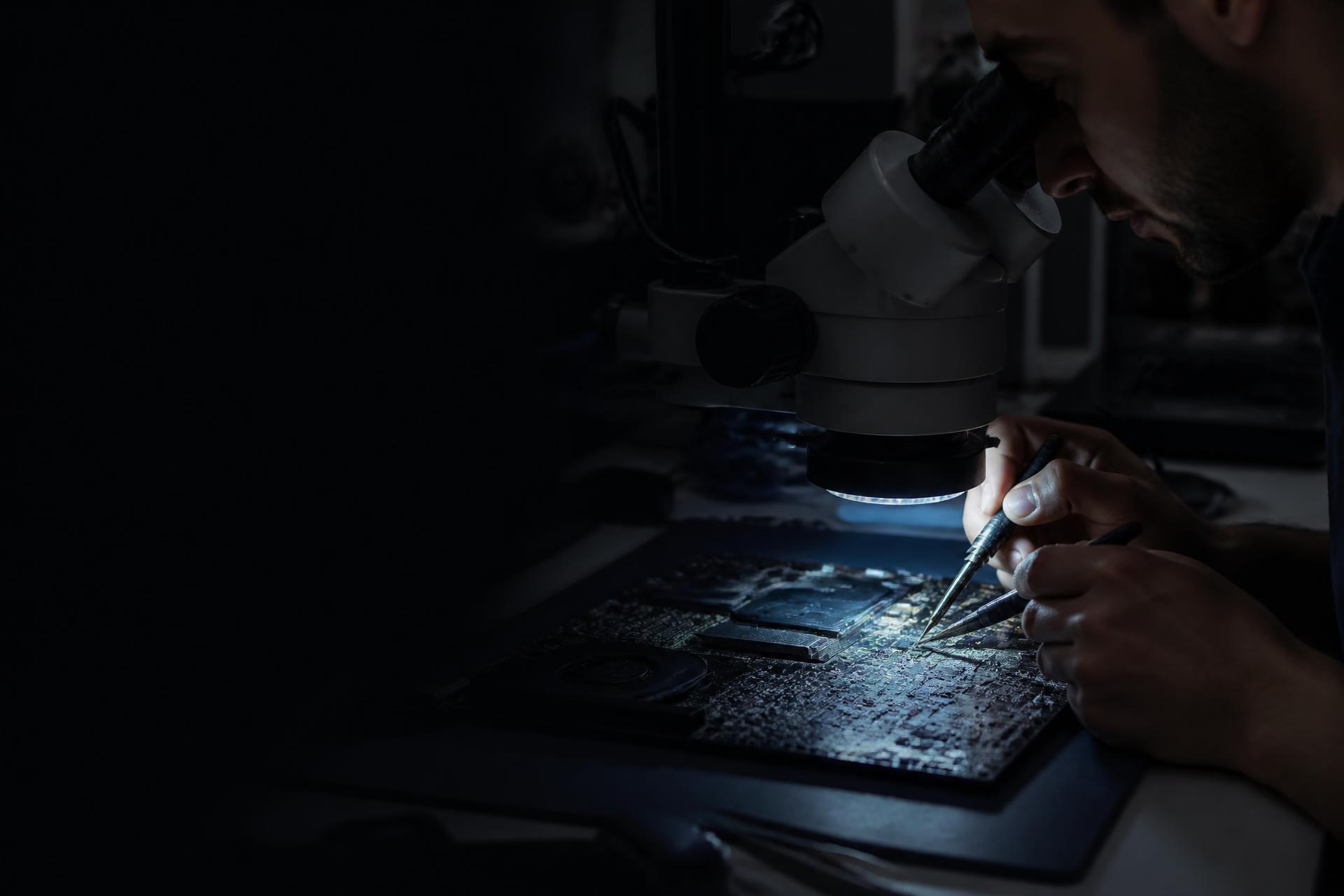 Technician performing precise logic-board microsoldering under magnification